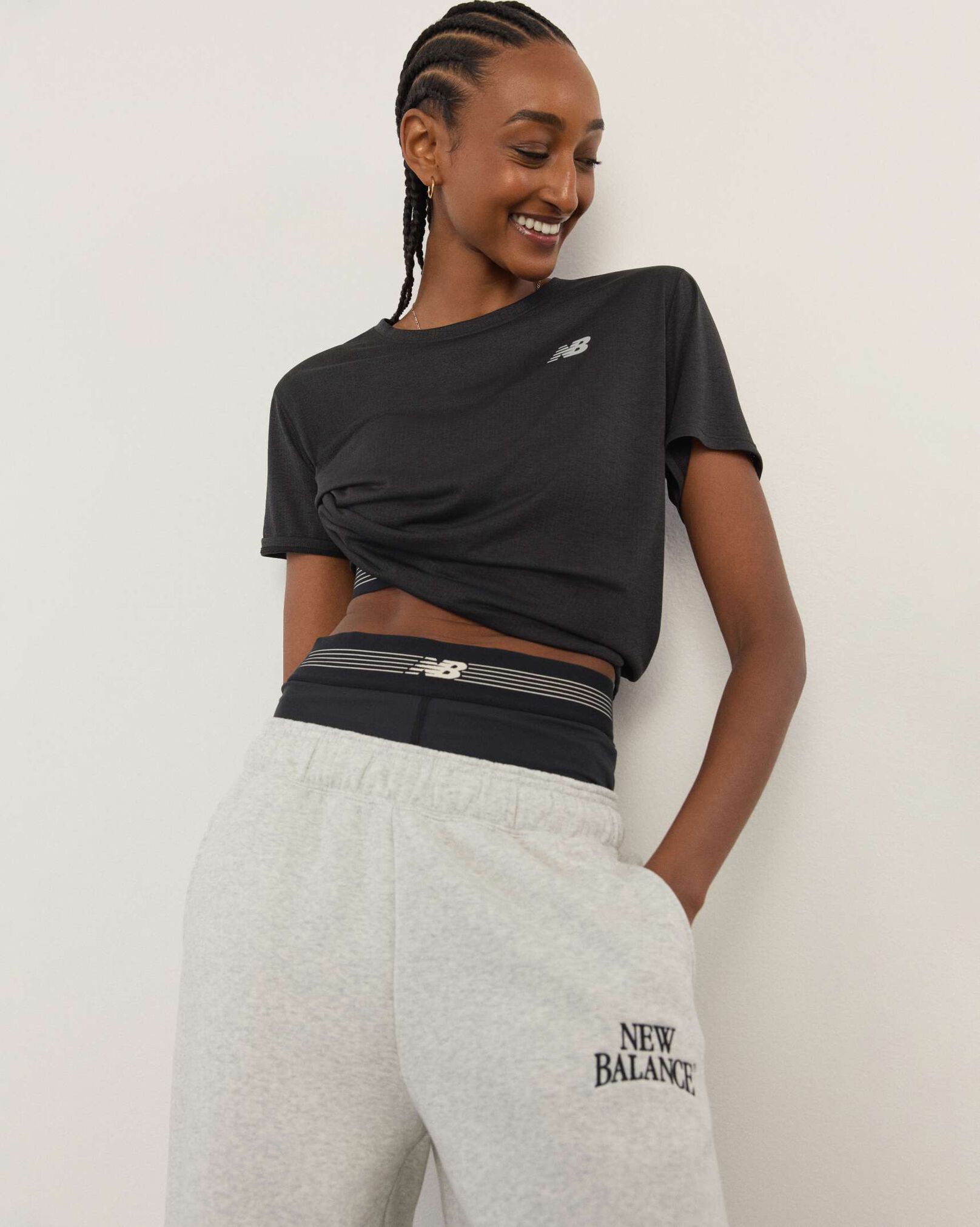 A woman wearing New Balance standing in front a white wall.