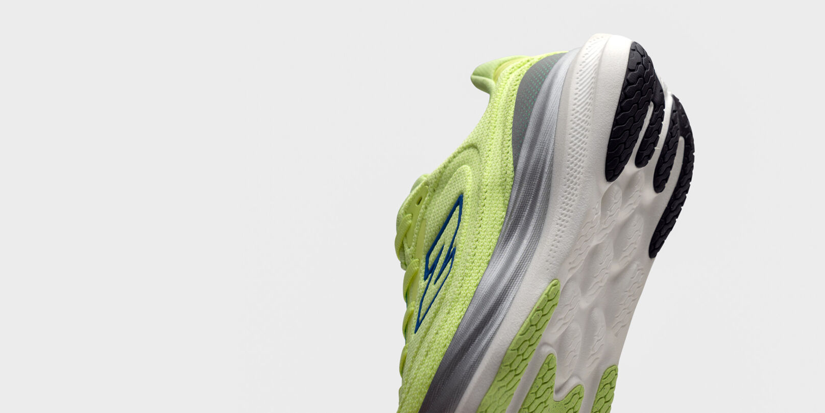 Close-up of the heel and sole of a bright yellow-green New Balance running shoe with blue logo, gray accents, and white sole featuring black tread. 