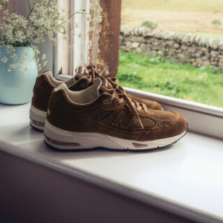 A pair of New Balance Made in UK sneakers sitting in a white studio environment. 