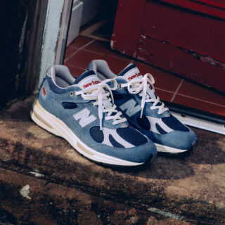 A pair of New Balance Made in UK sneakers in front of a rabbit in a brown textured studio environment. 
